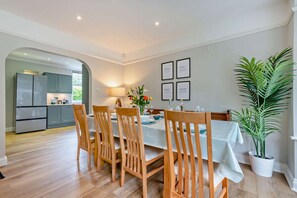 A dining area with a table set for four, wooden chairs, a potted plant, and framed pictures on the wall.