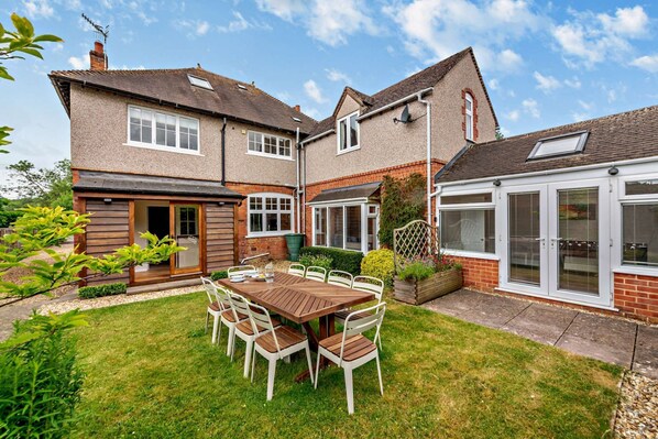 A two-story house with a patio area featuring a wooden table and chairs.