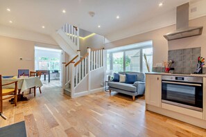 A modern kitchen with a built-in oven, a dining area with a table and chairs, and a staircase leading to an upper level.