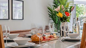 Une table à manger dressée avec des assiettes, des bols, des verres, un pain, une planche de charcuterie et un vase rempli de fleurs.