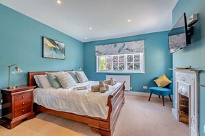 A bedroom with a bed, bedside table, dresser, window, and a fireplace.