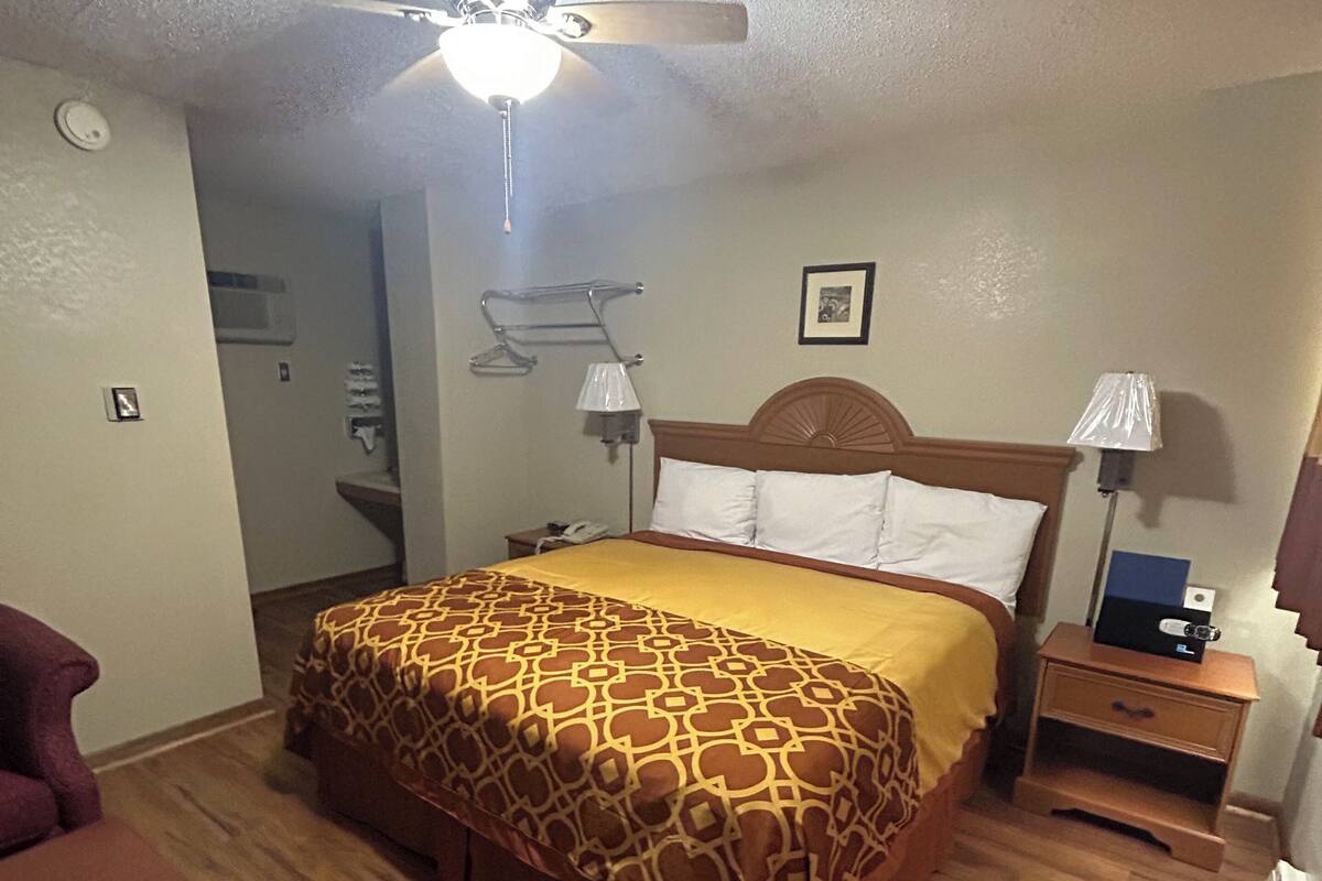 A hotel room with a bed, a ceiling fan, a nightstand, a lamp, and a chair.