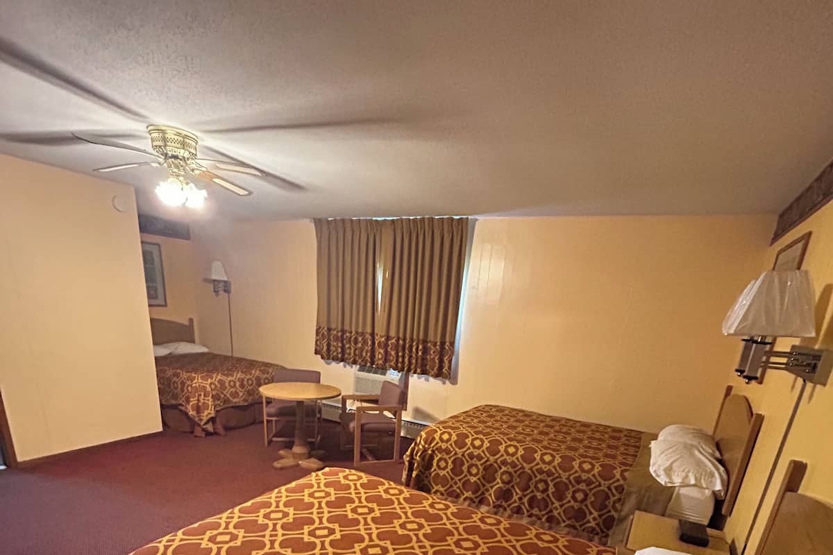 A hotel room with a bed, a desk, a chair, a ceiling fan, and a window with curtains.