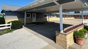 A motel with a covered parking area, a brick entrance, and a small garden with potted plants. - Royal Rest Motel  (Chariton)