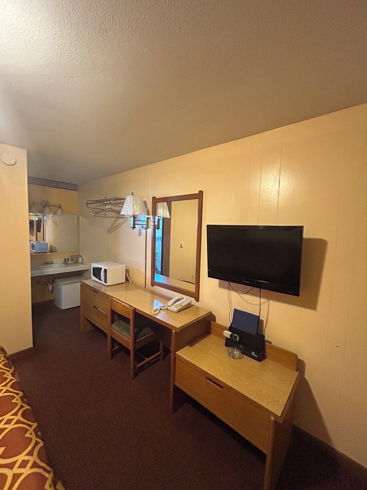Ein Hotelzimmer mit einem Bett, einem Schreibtisch mit Telefon, einem Fernseher und einem Spiegel.