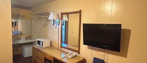 Ein Hotelzimmer mit einem Bett, einem Schreibtisch mit Telefon, einem Fernseher und einem Spiegel.