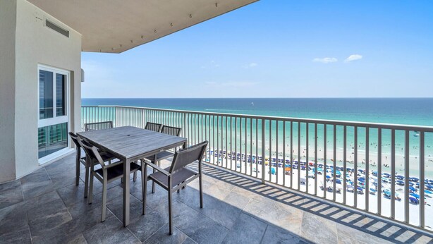 A balcony with a table and chairs, overlooking a beach with umbrellas and people. - Stunning Beach, Golf Course and Bay Views!  Empress 1103 (Miramar Beach)