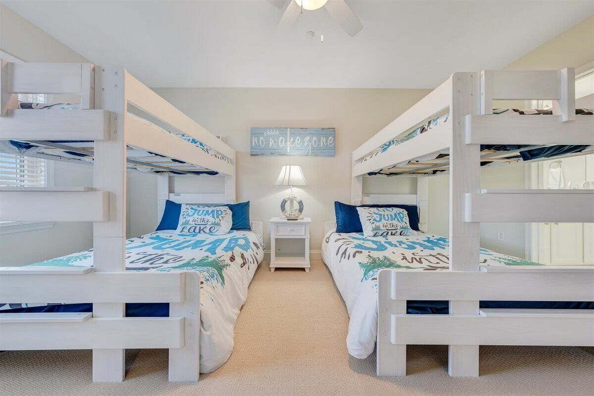 A bunk bed room with two beds, a nightstand, a lamp, and a wall sign.