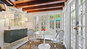 Un comedor con una mesa redonda, dos sillas, un armario y una ventana con vista a follaje.