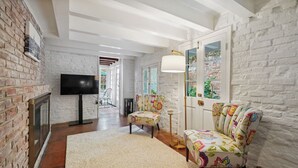 Una sala de estar con pared de ladrillo, chimenea, televisor, sofá y lámpara.