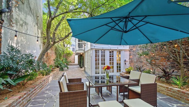 Un patio al aire libre con muebles de mimbre, una mesa con un jarrón de flores y un gran paraguas azul.