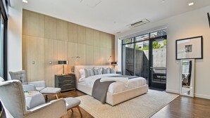 A modern bedroom with a large bed, grey upholstered chairs, a dark nightstand, and a large window offering a view of the outdoors. - Parkite on Main (Park City)