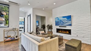 A modern living room with a fireplace, a large TV mounted on a textured wall, and a comfortable seating area. - Parkite on Main (Park City)
