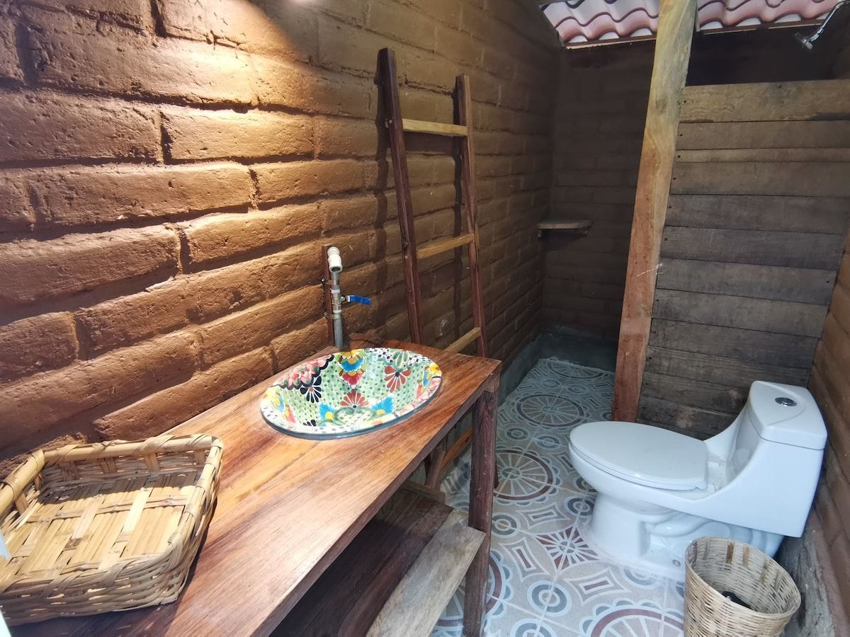 Ein rustikales Badezimmer mit einer Holzbank, einem farbenfrohen Waschbecken, einer weißen Toilette und einer Leiter an der Wand.