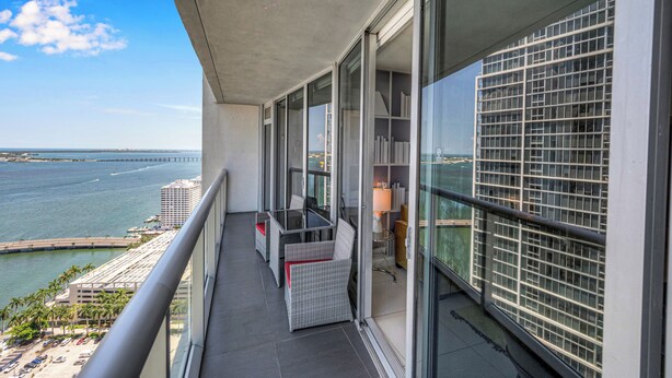 A balcony with a view of the ocean and a bridge, furnished with wicker chairs and a table. - Icon Luxury 34th Floor Amazing Oceanview, Brickell (Miami)