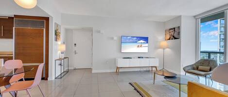 A modern living room with a TV, seating, and a view of the city.