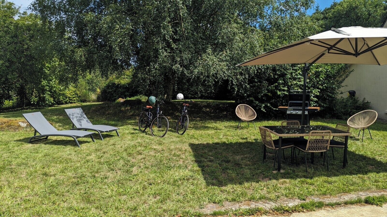 A grassy outdoor area with two lounge chairs, a table with chairs, a bicycle, and a large umbrella.