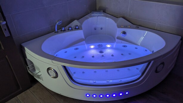 A modern spa tub with a built-in seat, multiple jets, and LED lighting. - Gîte Atypique Avec Services Tout Inclus, à L'orée D'une Forêt Privée (Le Mené)