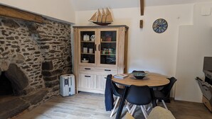 A cozy living area with a stone wall, a wooden cabinet with glass doors, a round wooden table, and a black sofa. - Gîte Atypique Avec Services Tout Inclus, à L'orée D'une Forêt Privée (Le Mené)