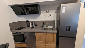 A compact kitchen with a built-in microwave, a stainless steel refrigerator, a sink, and wooden cabinets. - Gîte Atypique Avec Services Tout Inclus, à L'orée D'une Forêt Privée (Le Mené)