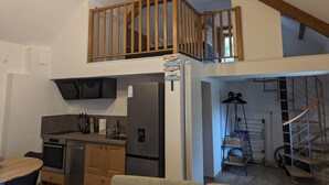 A modern kitchen with a built-in oven, a refrigerator, and a dining area with a table and chairs. - Gîte Atypique Avec Services Tout Inclus, à L'orée D'une Forêt Privée (Le Mené)