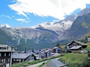 Un pueblo de montaña con casas tradicionales, una carretera visible y un hotel llamado "Hotel Alpenblick".