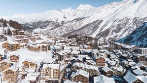Un village de montagne enneigé, avec des bâtiments en bois et un ciel d’un bleu limpide.