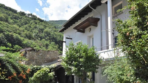 A traditional stone building with a white facade, surrounded by lush greenery and a stone pathway leading to the entrance. - La Casa del Nonno by Interhome (Valtellina)