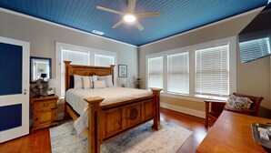 A bedroom with a wooden bed, a ceiling fan, and large windows with blinds.
