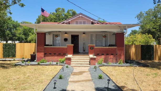A two-story house with a red brick facade, a welcoming front door, and a small porch with hanging flower baskets.