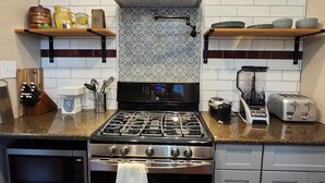 A modern kitchen with stainless steel appliances, a microwave, oven, and a gas stove. There are wooden shelves with dishes and a coffee maker on the counter.