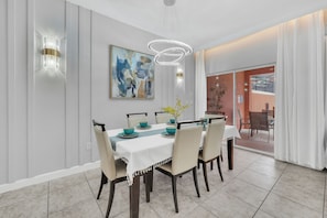 Un comedor con una mesa blanca dispuesta para seis personas, sillas color beige y una lámpara de techo moderna.
