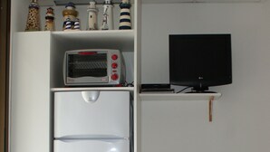 Cocina compacta con refrigerador blanco, microondas y televisor de pantalla plana sobre una estantería.