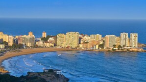 A coastal cityscape with high-rise buildings, a beach, and a rocky outcrop.