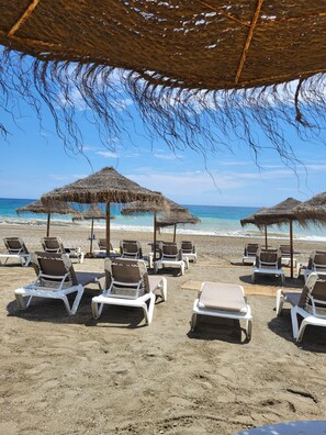 A beach with thatched umbrellas and white lounge chairs. - Beachfront 3 Bed Apt San Luis De Sabinillas (San Luis de Sabanillas)