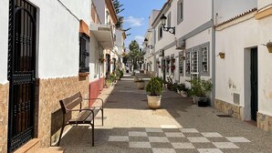 A narrow street with buildings on either side, benches, and potted plants. - Beachfront 3 Bed Apt San Luis De Sabinillas (San Luis de Sabanillas)