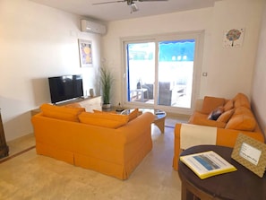Una sala de estar con sofá, mesa de centro, televisor y un amplio ventanal.