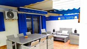 An outdoor patio with a table and chairs, an air conditioning unit, and a blue awning. - Beachfront 3 Bed Apt San Luis De Sabinillas (San Luis de Sabanillas)