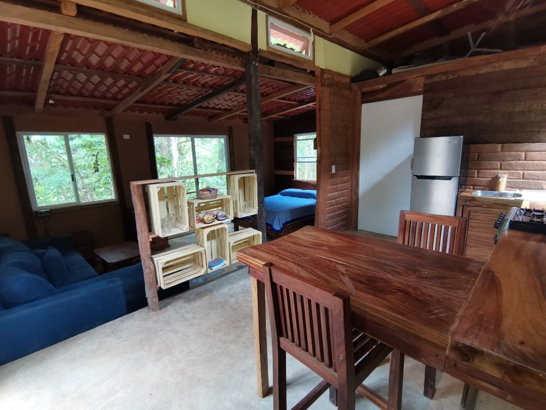 L’intérieur d’un chalet rustique comprend une table à manger, des chaises, un canapé, un lit et un réfrigérateur.
