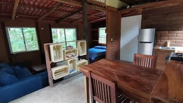 L’intérieur d’un chalet rustique comprend une table à manger, des chaises, un canapé, un lit et un réfrigérateur.