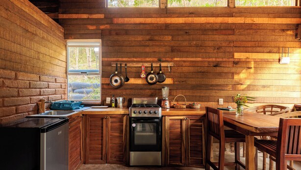 A rustic kitchen with wooden walls, a stove, oven, and a sink.