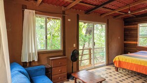 A room with a wooden ceiling, a bed with a striped bedspread, a blue sofa, a wooden nightstand, and a fan.