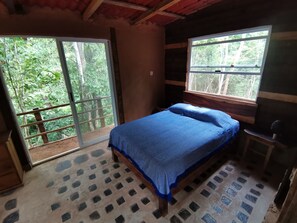 A bedroom with a bed, a window, and a view of greenery outside.