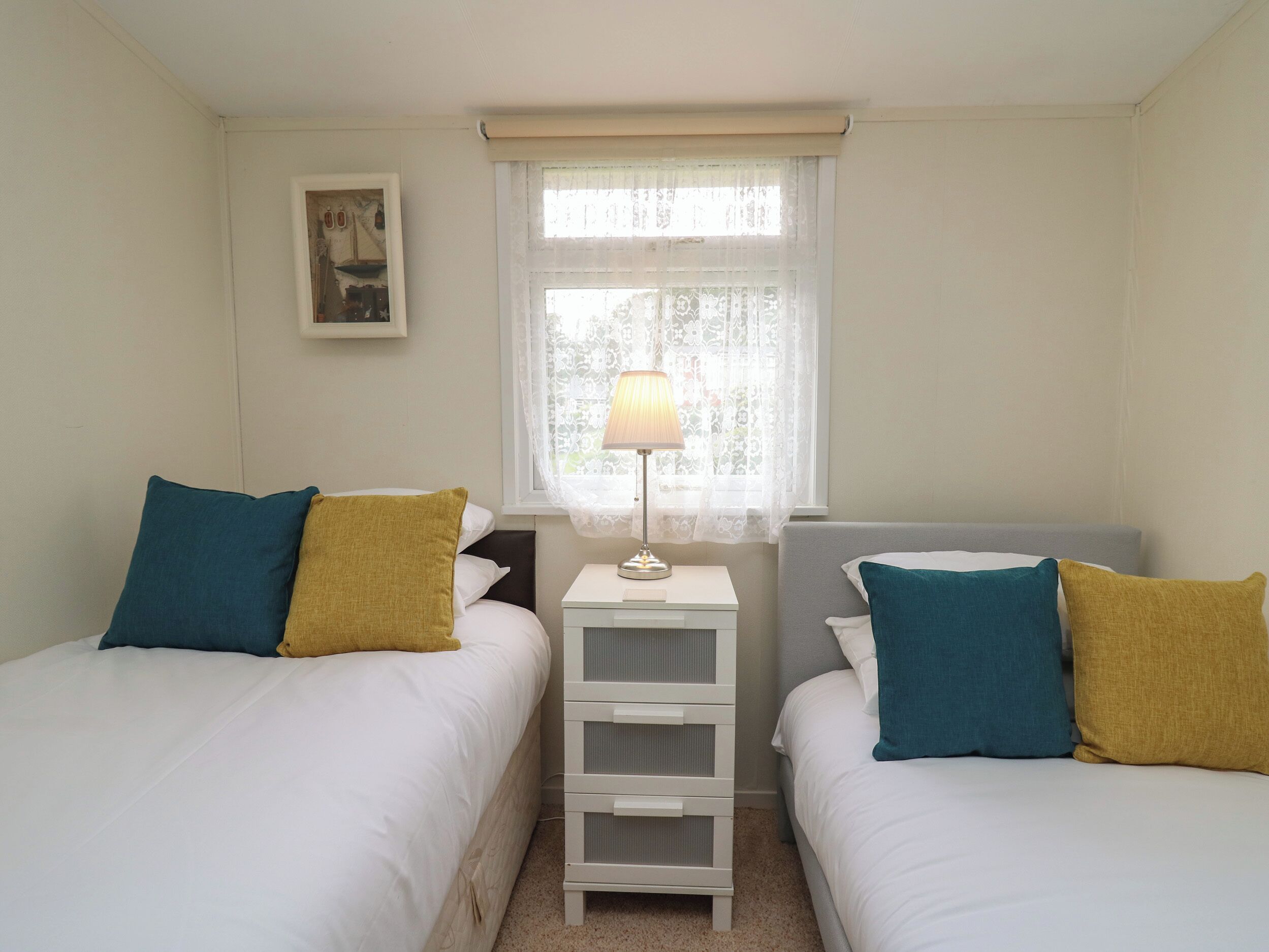 A bedroom with two beds, each with a pillow and a bedside table with a lamp.