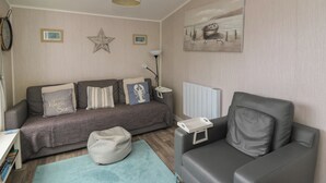 A cozy living room with a grey sofa, a bean bag, a small table, and a radiator. - Chalet 64 (Tywyn)