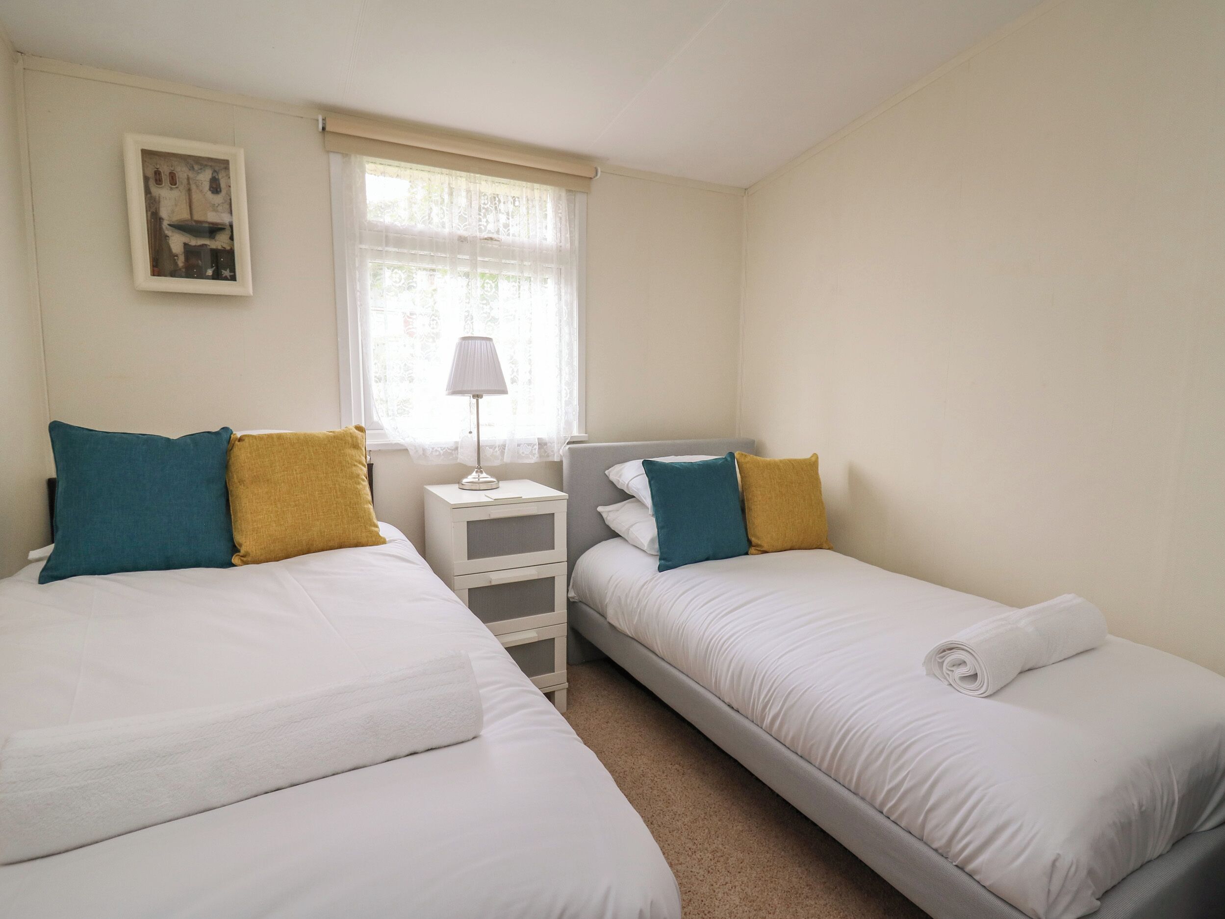 A twin room with two beds, a nightstand, a lamp, and a window with sheer curtains.