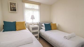 A twin room with two beds, a nightstand, a lamp, and a window with sheer curtains.