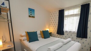 A neatly made bed with a blue and white striped pillow, a teal pillow, and a folded towel. - Chalet 64 (Tywyn)