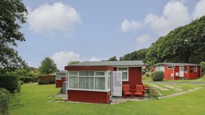 A red single-story building with a small porch and a window. - Chalet 64 (Tywyn)