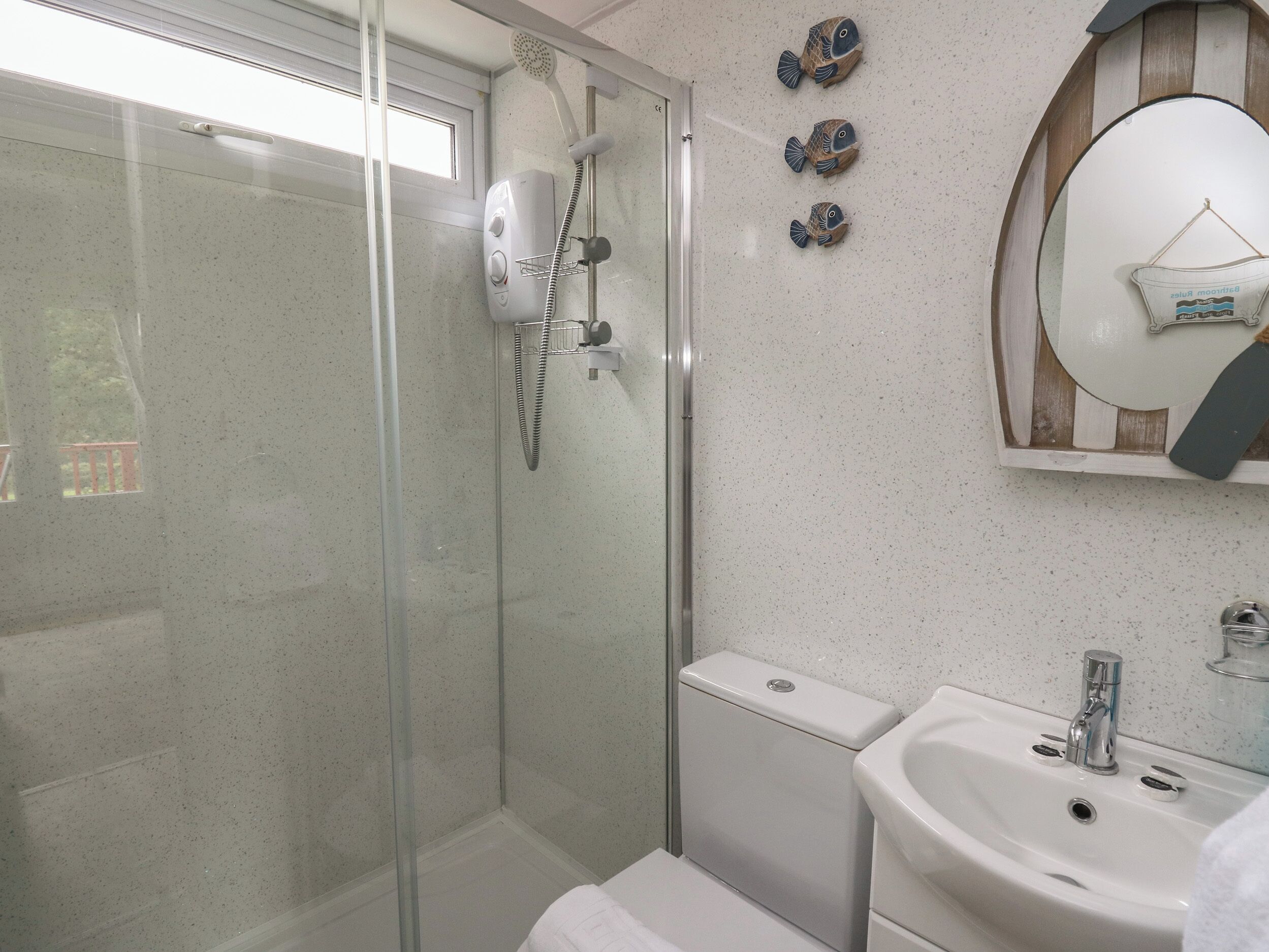 A modern bathroom with a glass-enclosed shower, a white sink, and decorative fish wall art.